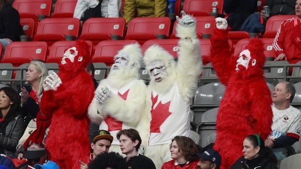 Four people wearing red and white Sasquatch costumes stand up in the crowd at a rugby event.