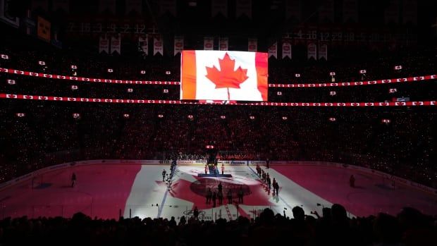 Players and fans stand for the Canadian national anthem at an arena.