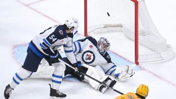 A puck goes into the net with two players in front. 