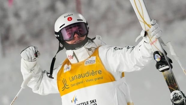 A male freestyle skier pumps his right fist in celebration while holding skis in his left hand.