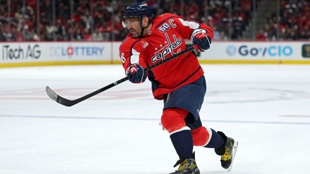 A male ice hockey player takes a slap shot in an arena filled with fans.