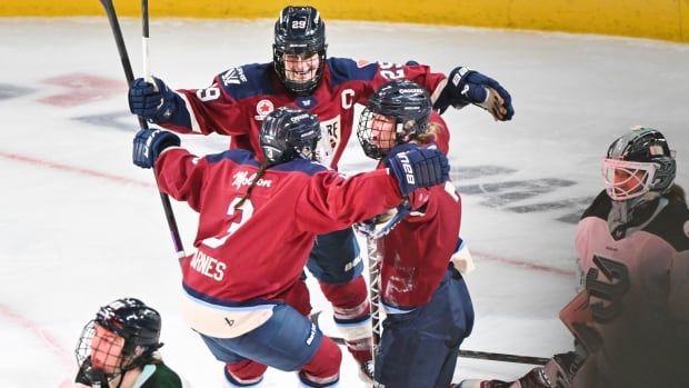 Three female ice hockey players wrap their arms around each other in celebration during a game.