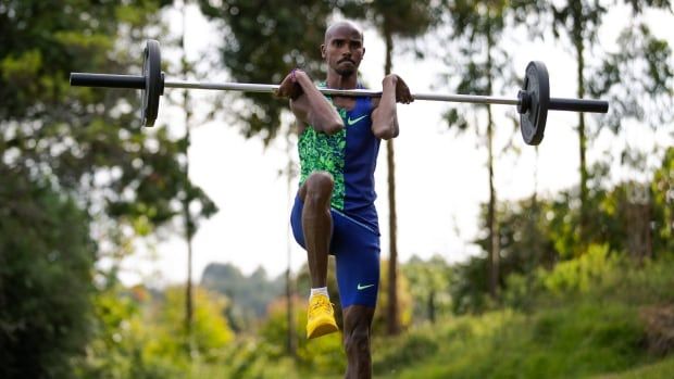 Male long distance runner, lifts one knee to waist with a barbell held at shoulders during training.