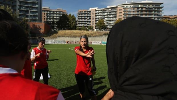 A woman wearing a red soccer jersey standing in the centre talks to other women on a field.