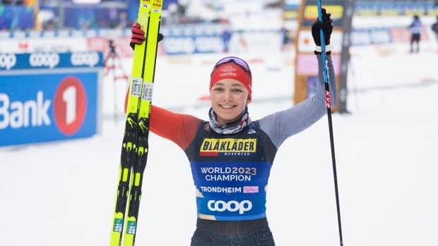 A female Para cross-country skier smiles while raising her skis in celebration after a race.