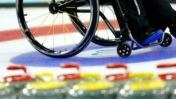 Close up of lower half of a wheelchair on curling ice with blurred curling rocks in the bottom of the frame.