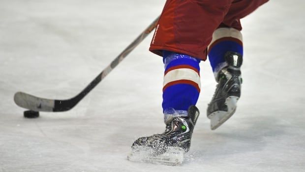 A closeup shows the skates of a hockey player handling a puck with a stick.