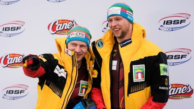 Two male sliders celebrate their win, posing with smiles and dressed in winter coats after their race.