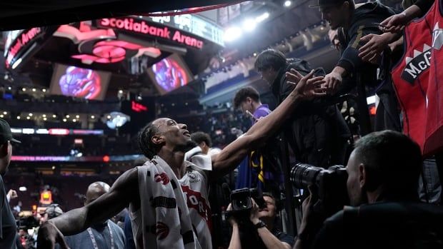 A basketball player greets fans in the stands as he walks off the court.