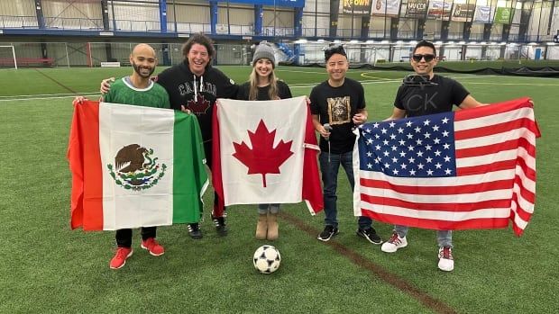 A group of people stand on a soccer field, holding flags for Mexico, Canada and the US.