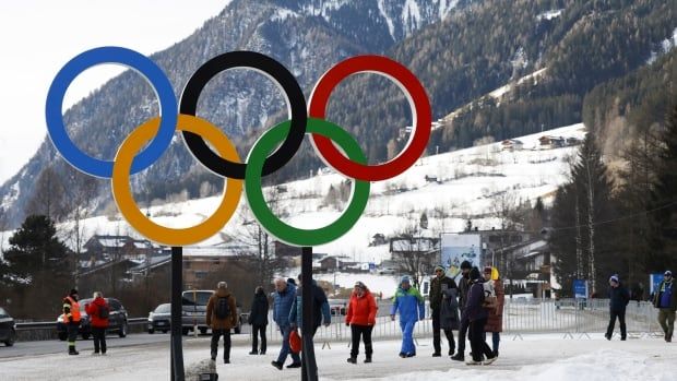 People walk near the Olympic rings in a snow-covered setting.