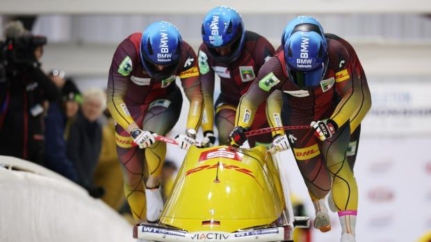 Four male bobsleigh athletes push sled on the track at the start of the race.