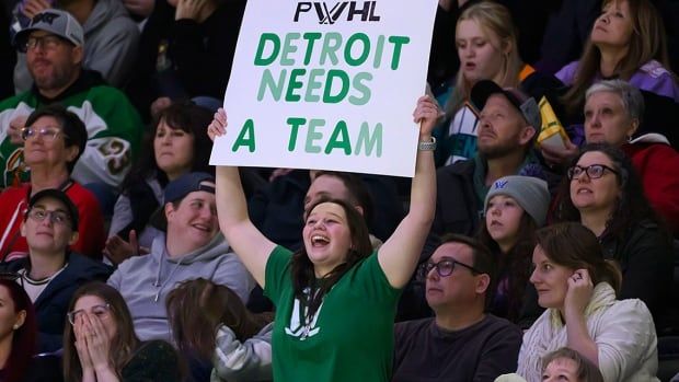 A fan holds up a sign indicating a desire for Detroit to get a Professional Women’s Hockey League team during the second period of regular-season neutral site game between the New York Sirens and Minnesota Fros at Little Caesars Arena on March 16, 2025. 