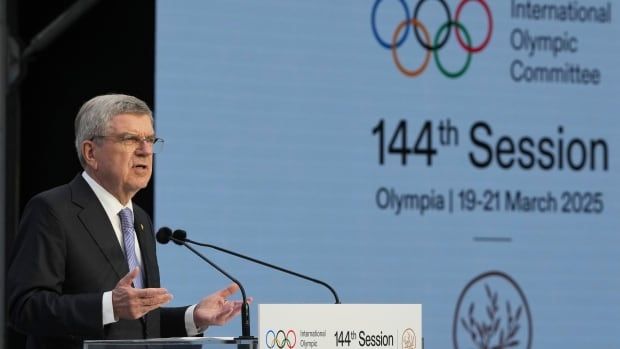 A man speaks at a podium, with a white background behind him that says "International Olympic Committee, 144th Session." 