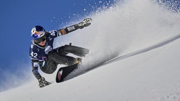 A women's snowboarder speeds down a hill while a spray of snow trails behind her.