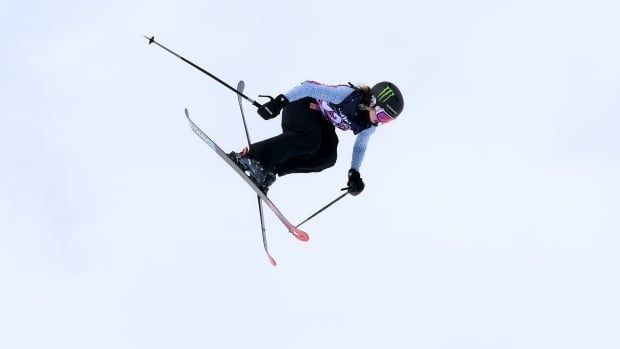 Female freestyle skier is airborne with skis pointing down, ready to land.