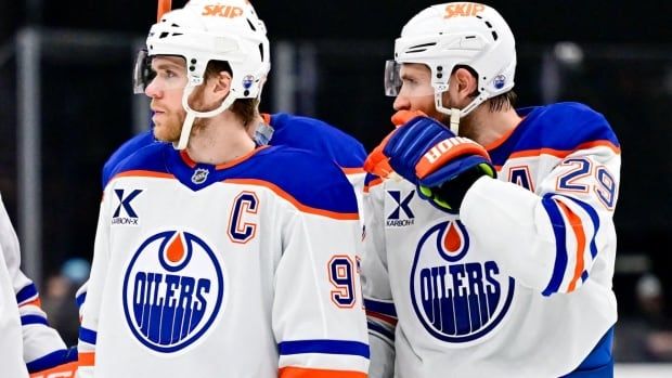 Two male ice hockey teammates stand alongside each other on the ice.