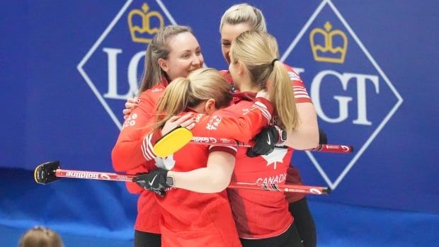 A four-woman curling team wraps their arms around each other on the ice in celebration.